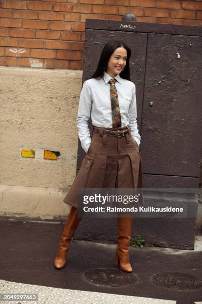 Yoyo Cao wears brown long boots, brown pleated midi skirt, pale blue shirt and a tie outside Chloe during the Womenswear Fall/Winter 2024/2025 as...