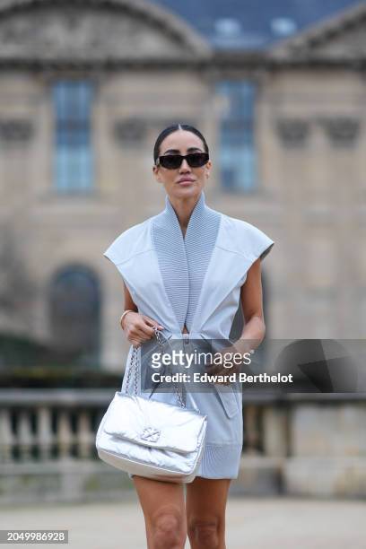 Tamara Kalinic wears sunglasses, a pastel pale blue mini gathered dress with pagoda sleeves and ribbed lapels, a silver shiny leather puff bag,...