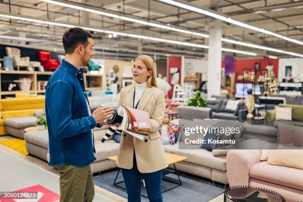 a saleswoman is talking to a handsome man in a furniture store, who is choosing the material and color for his new furniture - loja de móveis imagens e fotografias de stock