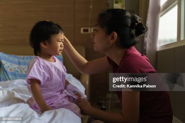 asian little boy with saline intravenous drip crying and sitting in the hospital bed while mother consoling and hugging him. adorable asian kids get sick from virus and hospitalized. baby health care medical concept. - moms crying in bed stock pictures, royalty-free photos & images