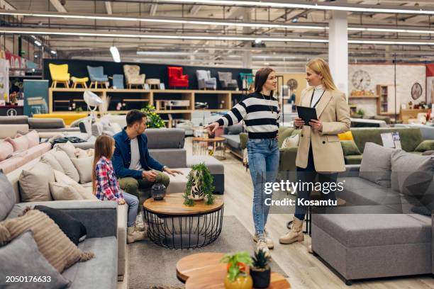 while the father and daughter are sitting on the sofa bed in the shop, the mother is talking to the friendly saleswoman - loja de móveis imagens e fotografias de stock