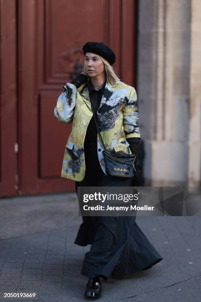 Karin Teigl seen wearing H&M black baret hat, H&M Studios black blouse / shirt, Stine Goya blue / green metallic print pattern blazer jacket, H&M...