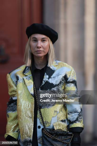 Karin Teigl seen wearing H&M black baret hat, H&M Studios black blouse / shirt, Stine Goya blue / green metallic print pattern blazer jacket and...