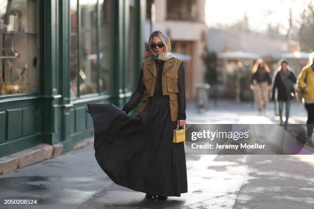 Karin Teigl seen wearing Loewe gold / brown tortoise sunglasses, H&M Studios colorful silk scarf, H&M Studios black blouse / shirt, H&M Studios khaki...