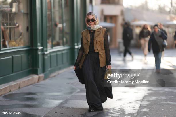 Karin Teigl seen wearing Loewe gold / brown tortoise sunglasses, H&M Studios colorful silk scarf, H&M Studios black blouse / shirt, H&M Studios khaki...