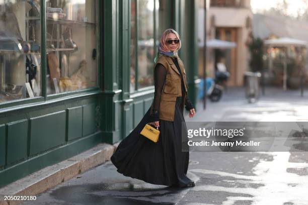 Karin Teigl seen wearing Loewe gold / brown tortoise sunglasses, H&M Studios colorful silk scarf, H&M Studios black blouse / shirt, H&M Studios khaki...