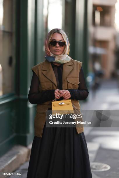 Karin Teigl seen wearing Loewe gold / brown tortoise sunglasses, H&M Studios colorful silk scarf, H&M Studios black blouse / shirt, H&M Studios khaki...