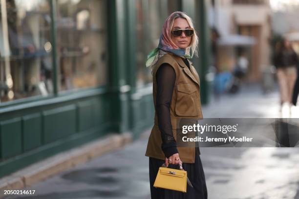 Karin Teigl seen wearing Loewe gold / brown tortoise sunglasses, H&M Studios colorful silk scarf, H&M Studios black blouse / shirt, H&M Studios khaki...