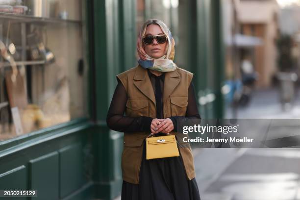 Karin Teigl seen wearing Loewe gold / brown tortoise sunglasses, H&M Studios colorful silk scarf, H&M Studios black blouse / shirt, H&M Studios khaki...