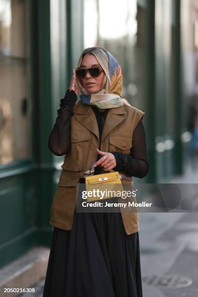 Karin Teigl seen wearing Loewe gold / brown tortoise sunglasses, H&M Studios colorful silk scarf, H&M Studios black blouse / shirt, H&M Studios khaki...