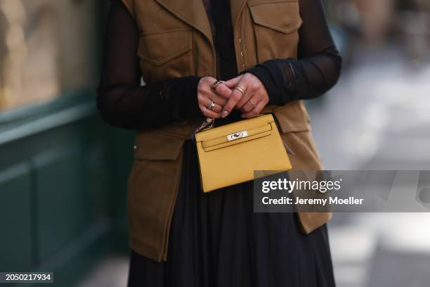 Karin Teigl seen wearing H&M Studios black blouse / shirt, H&M Studios khaki green utility gilet, gold rings, H&M Studios black oversized long maxi...