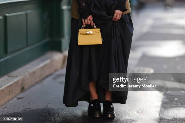 Karin Teigl seen wearing H&M Studios khaki green utility gilet, gold rings, H&M Studios black oversized long maxi skirt, Hermès yellow leather mini...