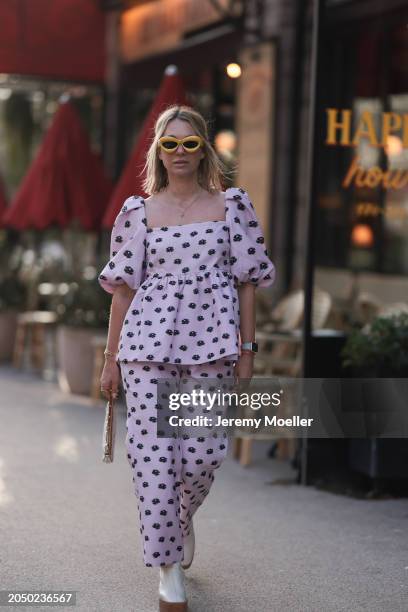 Karin Teigl seen wearing Loewe yellow sunglasses, gold necklaces, Stine Goya pink with black flower print pattern top with puffy sleeves, matching...