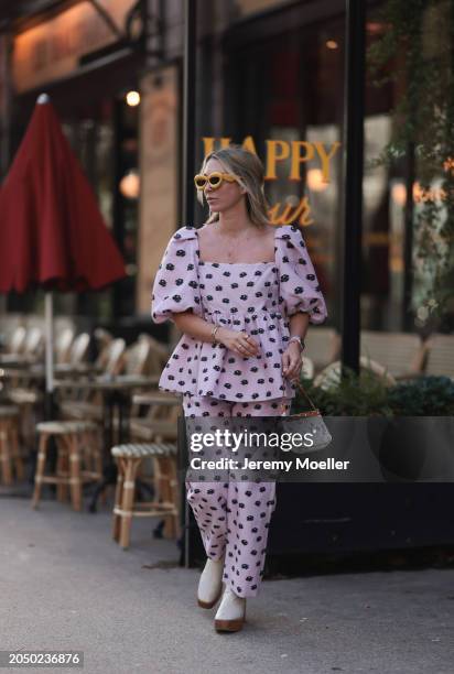 Karin Teigl seen wearing Loewe yellow sunglasses, gold necklaces, Stine Goya pink with black flower print pattern top with puffy sleeves, matching...