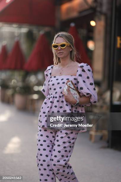 Karin Teigl seen wearing Loewe yellow sunglasses, gold necklaces, Stine Goya pink with black flower print pattern top with puffy sleeves, matching...