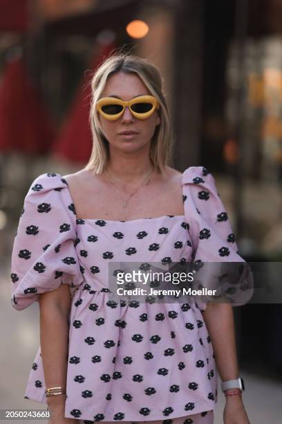 Karin Teigl seen wearing Loewe yellow sunglasses, gold necklaces, Stine Goya pink with black flower print pattern top with puffy sleeves, during the...