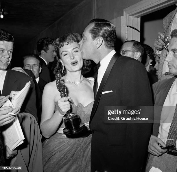 American actress Donna Reed kissed by American actor William Holden as they attend the 26th Academy Awards, held at the Pantages Theatre in the...