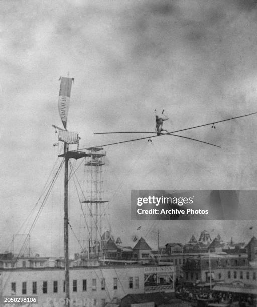 French acrobat and tightrope walker Charles Blondin stands on his head while performing a tightrope walk over Coney Island in the borough of...