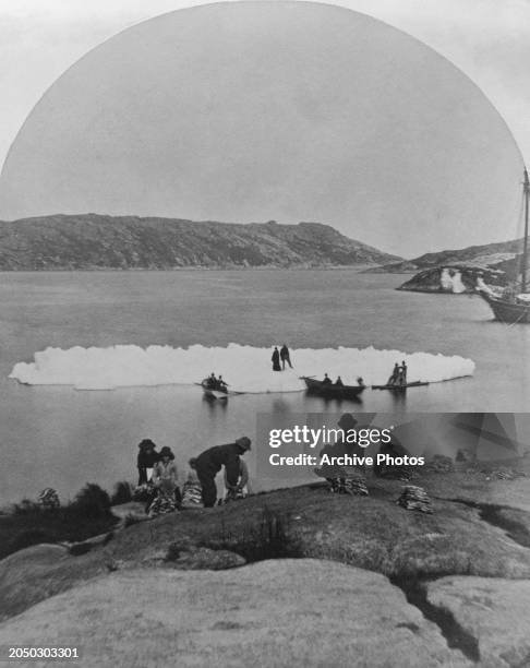 Innu peoples on an iceberg as others cure fish on the shore, at Pinsent's Arm , on the south side of St Michael's Bay, Newfoundland and Labrador,...