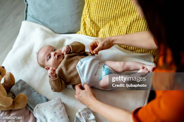 mujer joven cambiando su adorable pañal de bebé en una mesa en casa - pañal fotografías e imágenes de stock