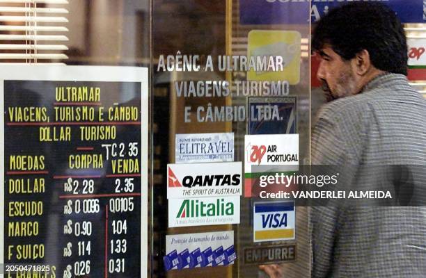 Client enters a currency exchange house with a sign in the store window that indicates the quotation of 2,35 reales to the dollar, 25 May 2001, in...