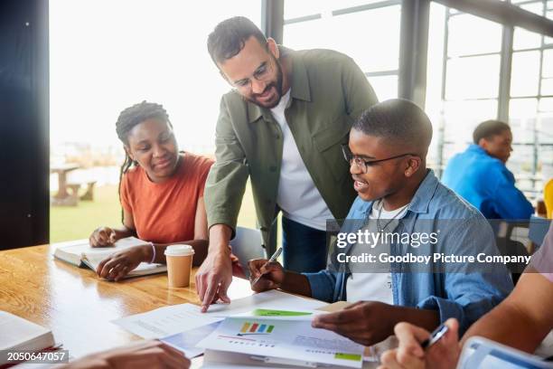 smiling teacher talking with college students studying around a cafeteria table - teachers break room stock pictures, royalty-free photos & images