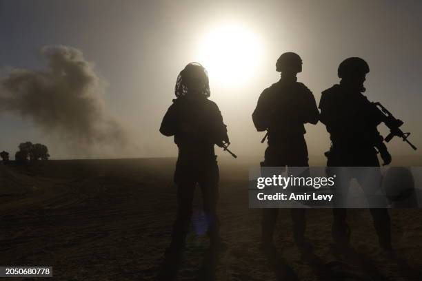 Soldiers with the Israel Defense Forces stand with their weapons as smoke rises from bombardments on Gaza on March 4, 2024 in southern Israel near...