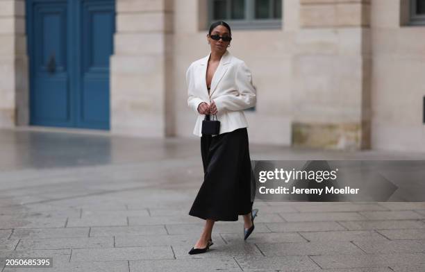 Cherifa Akili seen wearing YSL black sunglasses, silver earrings, Monceau white elegegant blazer jacket, Arket black oversized silk midi skirt, Amina...