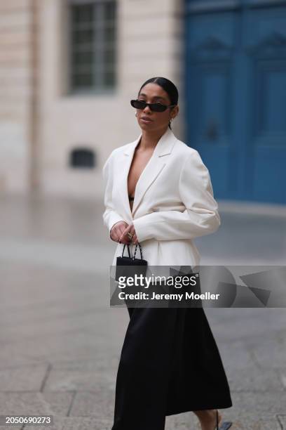 Cherifa Akili seen wearing YSL black sunglasses, silver earrings, Monceau white elegant blazer jacket, Arket black oversized silk midi skirt, Amina...
