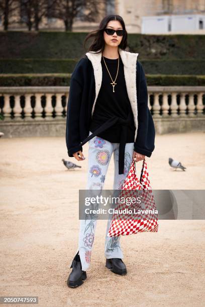 Mika Schneider wears black top, blue jacket with cream fur details, flower printed jeans, black boots, red and white checked Maison Margiela bag,...