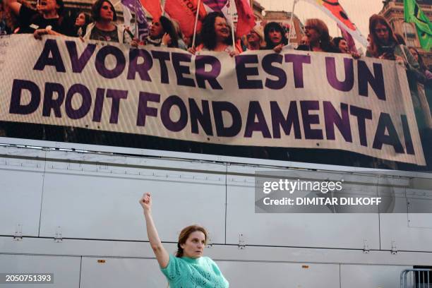 Woman clenches her fist as she dances in front of a screen displaying a slogan which reads "Abortion is a fundamental right" at the Place du...