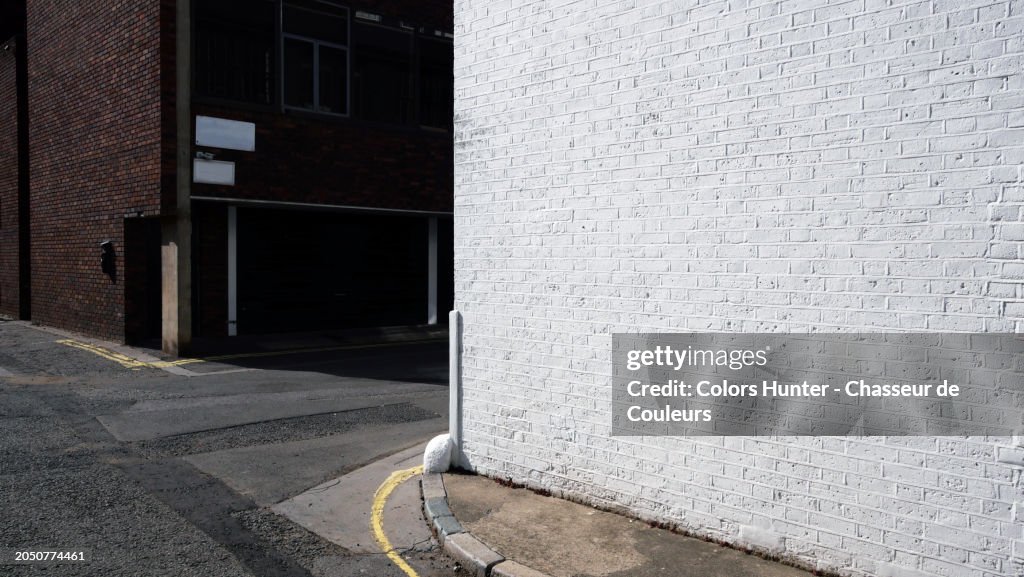 White brick wall on a street corner in London, England, United Kingdom. In the background, the rear facade of a residential building.
No people.
Sunlight. Natural colors.