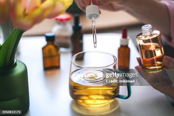 a woman putting medicine drops in a cup of tea. - cannabidiol stock pictures, royalty-free photos & images