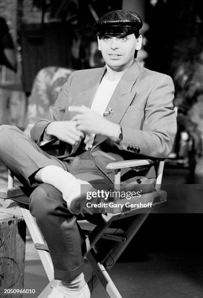 View of British New Wave musician Gary Numan as he sits in a director's chair during an interview on MTV at Teletronic Studios, New York, New York,...