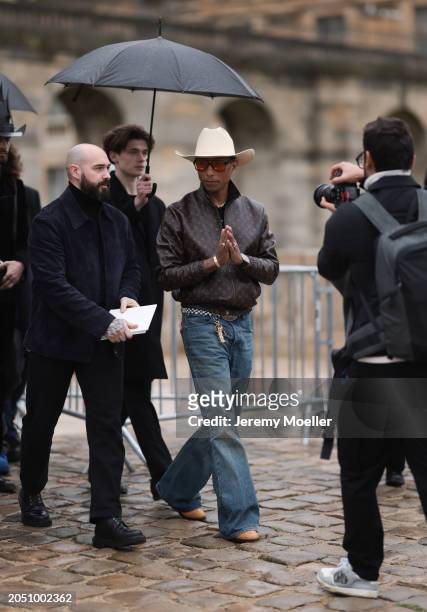 Pharrell Williams seen wearing beige large cowboy hat, black sunglasses with orange lenses, gold earrings and a gold necklace, Louis Vuitton brown...