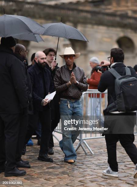 Pharrell Williams seen wearing beige large cowboy hat, black sunglasses with orange lenses, gold earrings and a gold necklace, Louis Vuitton brown...