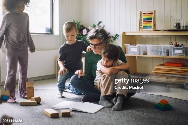 group of kids sitting with female teacher reading book in classroom at kindergarten - nursery school building stock pictures, royalty-free photos & images