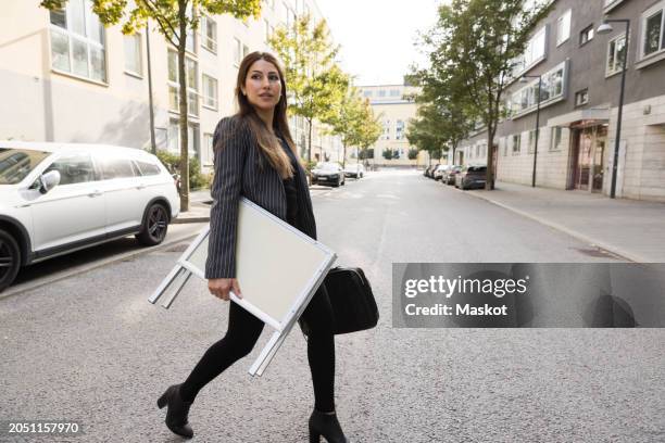 female real estate agent carrying placard while crossing street in city - carrying sign imagens e fotografias de stock