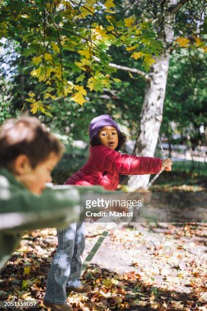 girl leaning on rope while playing with boy at park - stockholm park stock pictures, royalty-free photos & images