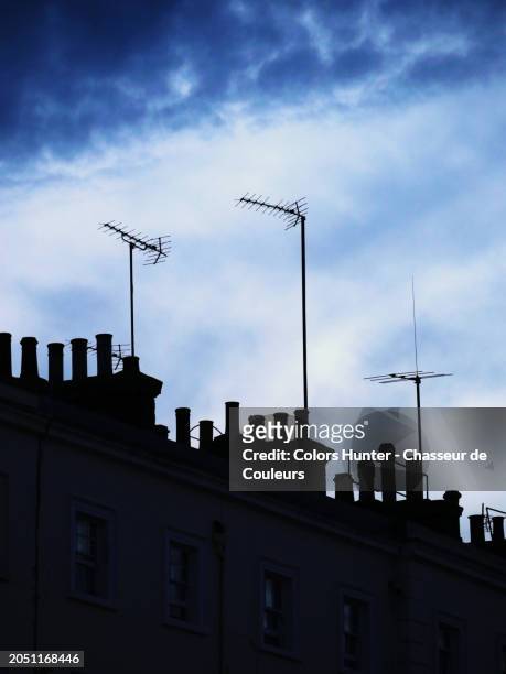 backlit view of rake antennas and chimneys on the roofs of residential buildings in london, england, united kingdom. sunlight. natural colors. blue and cloudy sky in the background. natural light and colors.
no people. - fear illustration stock pictures, royalty-free photos & images