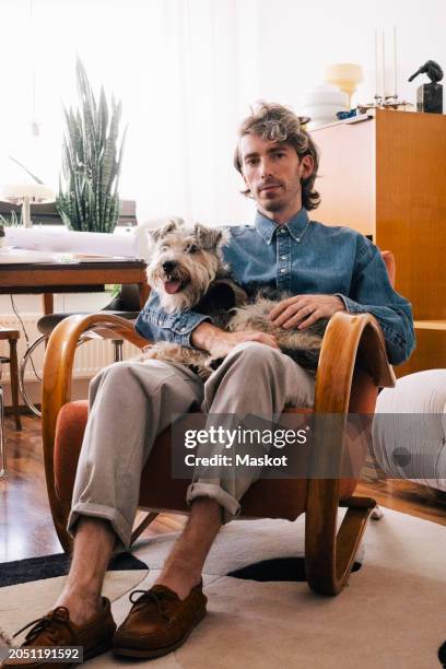 portrait of male architect carrying dog sitting on armchair at home office - designer einrichtung stock-fotos und bilder