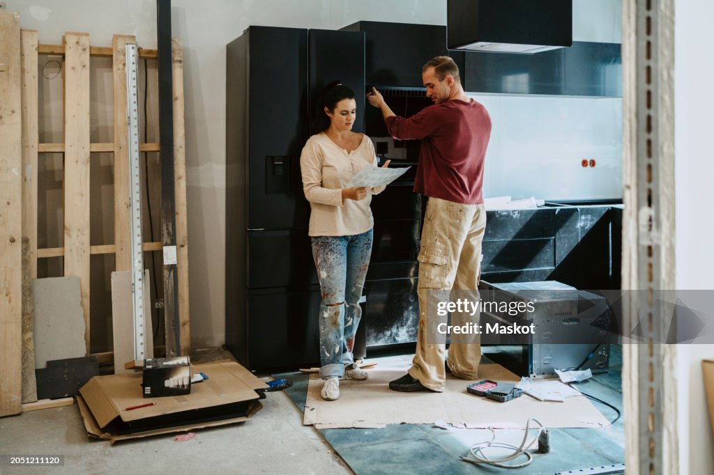 Couple discussing over document while fixing cabinet together in kitchen during home renovation