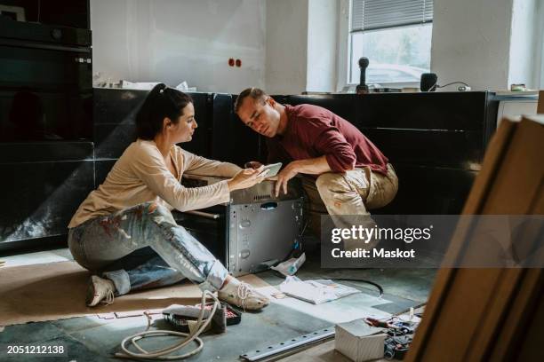 couple discussing over mobile phone while renovating kitchen at home - woman house renovation stock pictures, royalty-free photos & images