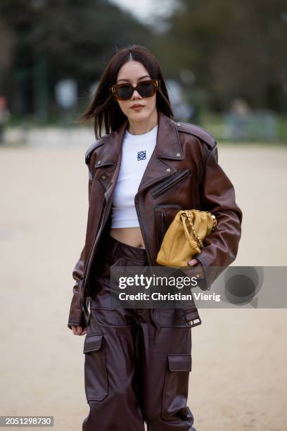 Jenny Tsang wears white cropped shirt with logo, brown leather jacket, pants with side pockets, beige Loewe flamenco bag outside Loewe during the...