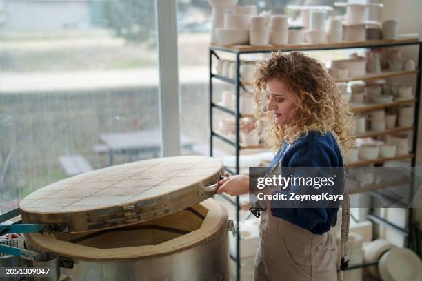 the woman is taking out ceramic pots from the ceramic kiln. - pottery kiln stock pictures, royalty-free photos & images