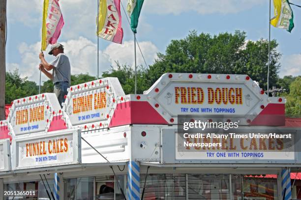 Patrick Wright of Brant, N.Y. Sets up the flags on top of the Fried Dough and Funnel Cakes business he works at the Altamont Fair on Sunday, Aug. 10,...