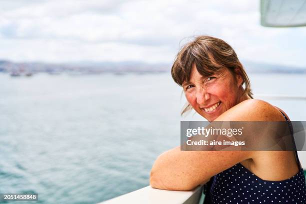 portrait of a female tourist in casual clothes smiling at the camera leaning on the handrail of a boat, side view - vigo stock pictures, royalty-free photos & images