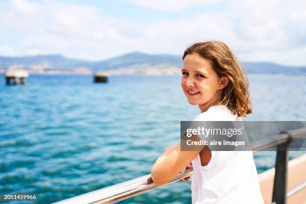 a smiling girl looking at the camera leaning against a steel railing illuminated by sunlight in the background is the sea. - vigo stock pictures, royalty-free photos & images