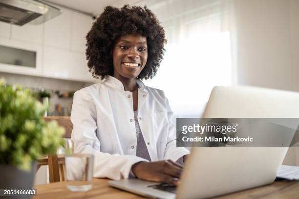 a young black female doctor conducting online consultations with patients via video call from her home office - social distancing hospital stock pictures, royalty-free photos & images