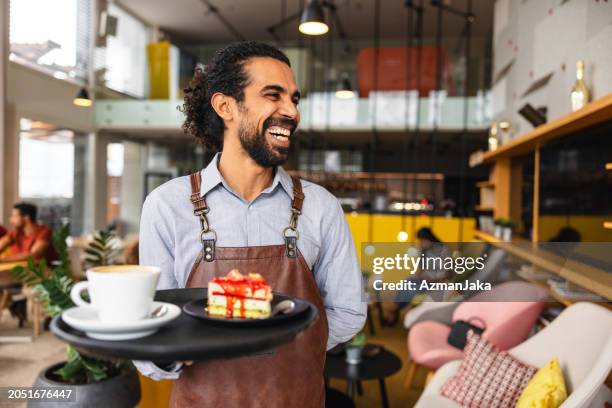 happy male middle eastern bartender laughing while carrying a tray with drinks at a bar - ober stockfoto's en -beelden